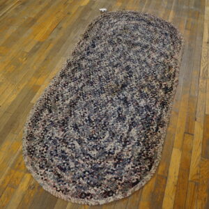 Oblong braided rug mixing navy, white, and red fibers rests on distressed yellow plank flooring.
