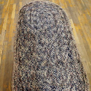A long, braided runner rug featuring variegated navy, gray, and tan colors covers old, worn hardwood flooring.