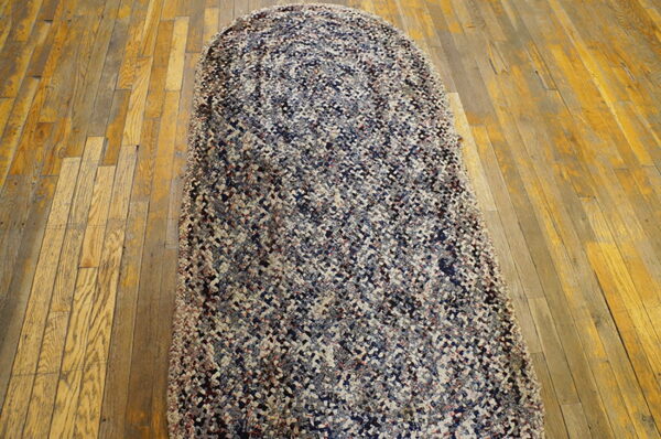 A long, braided runner rug featuring variegated navy, gray, and tan colors covers old, worn hardwood flooring.