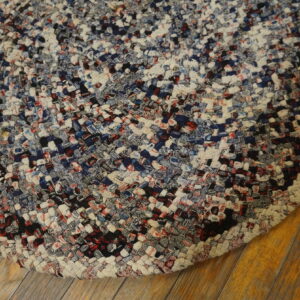 Braided rug featuring variegated navy, cream, black, and red textures resting on distressed wood planks.