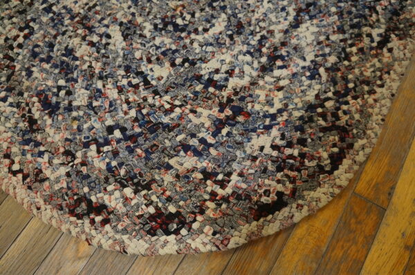 Braided rug featuring variegated navy, cream, black, and red textures resting on distressed wood planks.