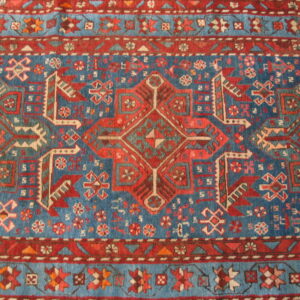 Detailed geometric rug pattern features saturated blue, rich reds, and cream tribal motifs.
