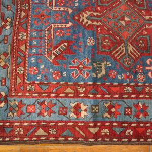 Geometric low pile rug in red and blue with complex borders lying on light brown wood flooring.