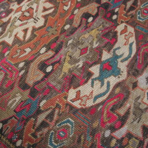 Textured close-up of a low pile rug displaying complex geometric patterns in brown, rust, beige, pink, and teal.
