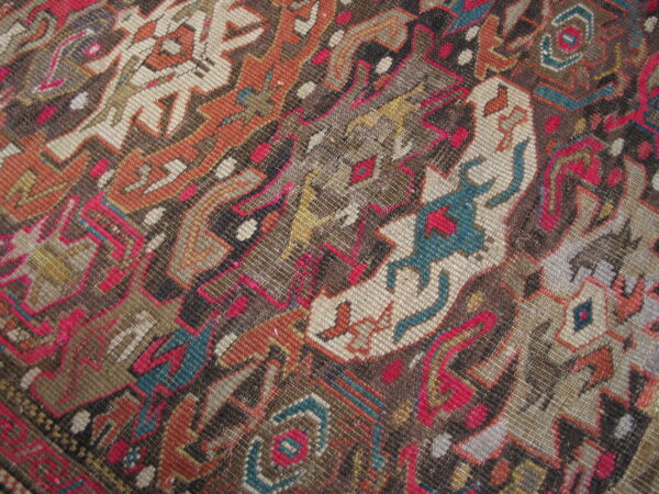 Textured close-up of a low pile rug displaying complex geometric patterns in brown, rust, beige, pink, and teal.
