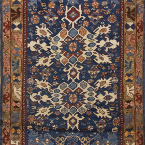 Deep blue rug with a cream and rust geometric design bordered by olive green and stylized traditional motifs.