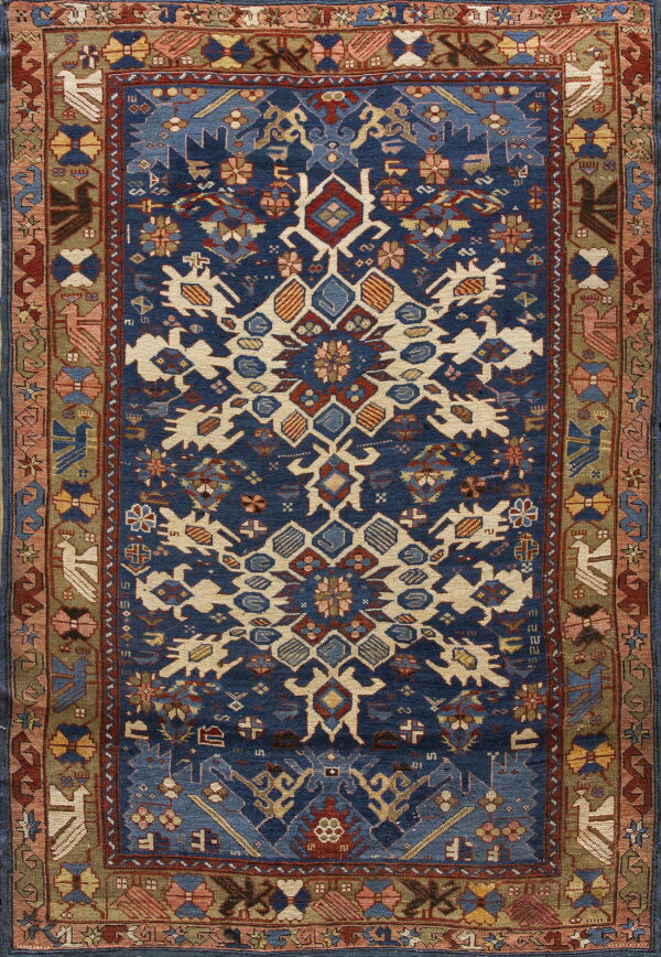 Deep blue rug with a cream and rust geometric design bordered by olive green and stylized traditional motifs.