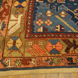 Geometric blue, terracotta, and olive green rug corner featuring a stylized bird pattern on a wood floor.