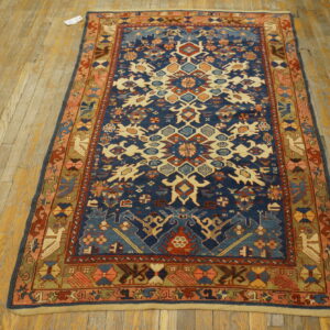 Low pile rug with geometric navy blue, cream, and rust patterns displayed on distressed wooden flooring.