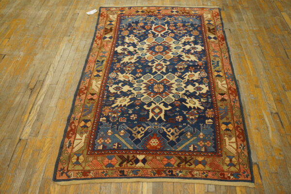 Low pile rug with geometric navy blue, cream, and rust patterns displayed on distressed wooden flooring.