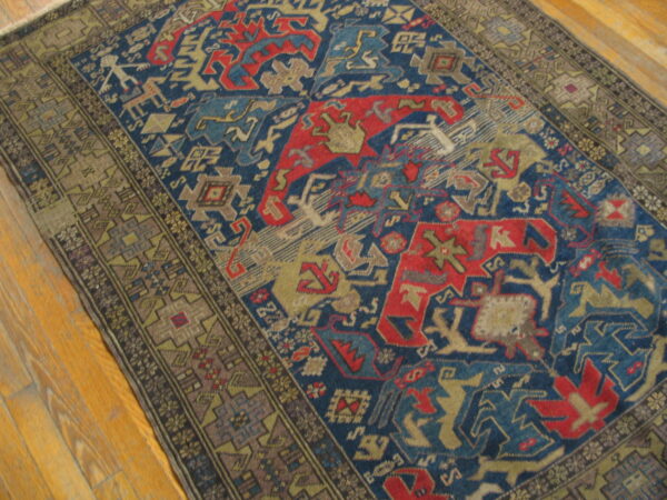 Low-pile rug with geometric blue, red, and taupe patterns resting on light plank wood flooring.