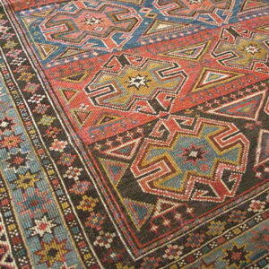 Close-up of a rug with geometric patterns in rust red, blue, dark brown, and gold.