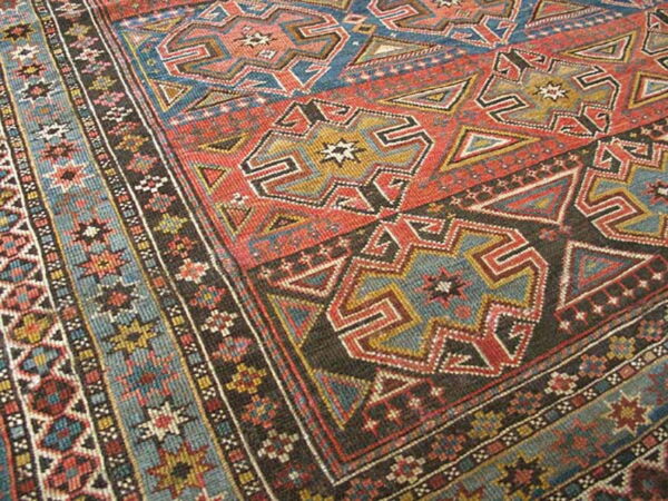 Close-up of a rug with geometric patterns in rust red, blue, dark brown, and gold.