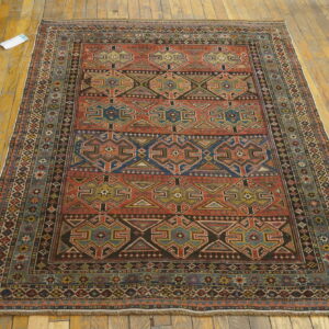 Geometric rust, blue, and black rug displayed flat on distressed golden hardwood flooring.