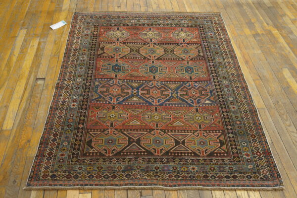 Geometric rust, blue, and black rug displayed flat on distressed golden hardwood flooring.