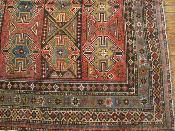 Geometric rug corner detail showing stepped designs in red, teal, black, and gold on a plank wood floor.