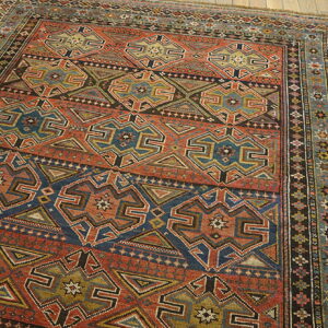 Rust and navy rug with geometric medallions and intricate borders on light plank wood flooring.