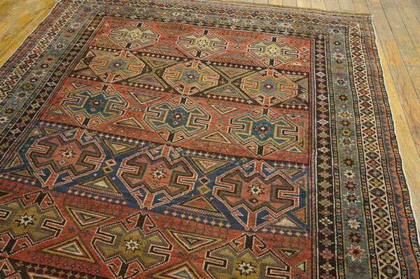 Rust and navy rug with geometric medallions and intricate borders on light plank wood flooring.