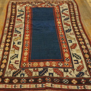 A blue center field rug with complex red, cream, and brown geometric borders on wood planks.