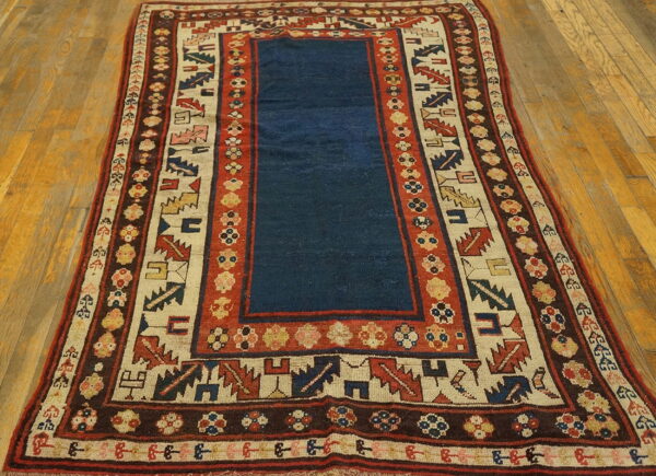 A blue center field rug with complex red, cream, and brown geometric borders on wood planks.