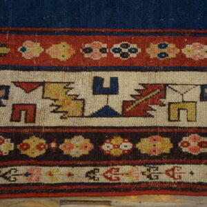 Detailed view of a low-pile rug border featuring geometric and floral motifs in blue, red, cream, and brown.