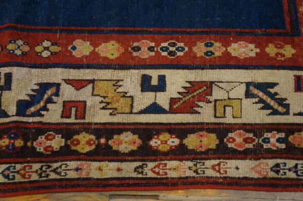 Detailed view of a low-pile rug border featuring geometric and floral motifs in blue, red, cream, and brown.
