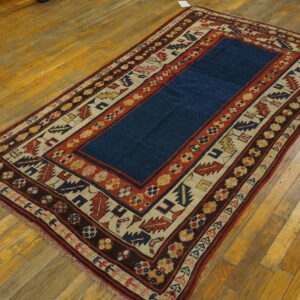 Low-pile rug featuring a navy center and highly patterned borders resting on distressed wooden planks.