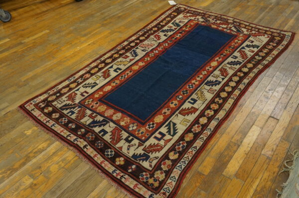 Low-pile rug featuring a navy center and highly patterned borders resting on distressed wooden planks.