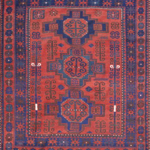 Rust-red rug with geometric navy blue medallions, framed by detailed borders and traditional motifs.
