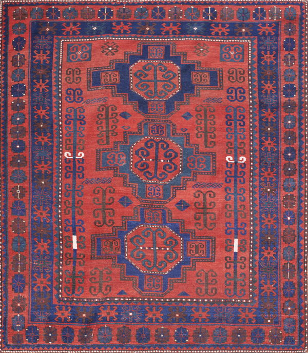 Rust-red rug with geometric navy blue medallions, framed by detailed borders and traditional motifs.