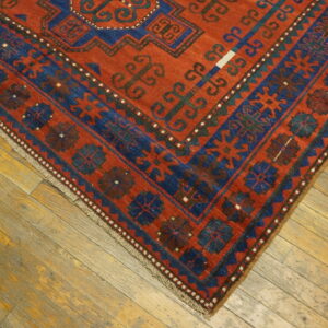 Detail of a rusty red and indigo rug with geometric tribal patterns laid over yellow-toned wooden planks.