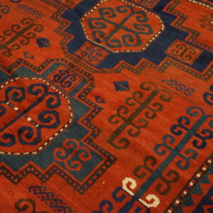 Geometric rug detail showing a rust-red field with navy and teal medallions and stylized scroll designs.
