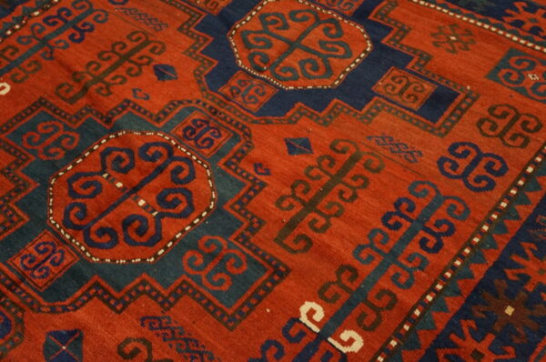 Geometric rug detail showing a rust-red field with navy and teal medallions and stylized scroll designs.