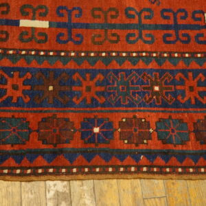 Geometric patterned rug in rich red, navy, and teal colors on light wooden floorboards.