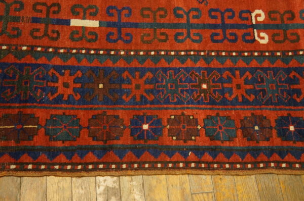 Geometric patterned rug in rich red, navy, and teal colors on light wooden floorboards.