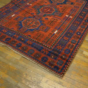 Red and blue geometric rug with medallions and elaborate borders rests on rustic wooden planks.