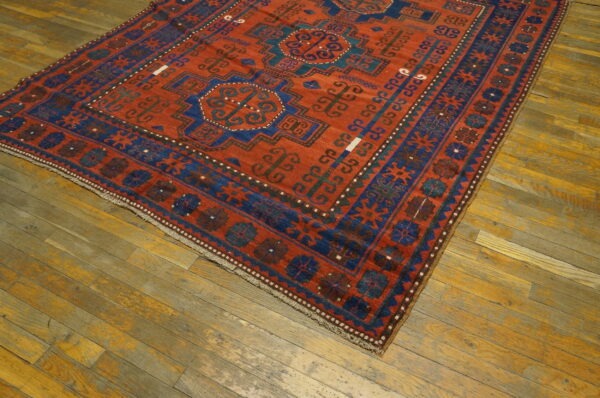 Red and blue geometric rug with medallions and elaborate borders rests on rustic wooden planks.