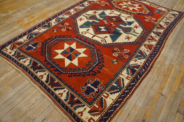 Low-pile rug in rust red, navy blue, and cream geometric patterns on distressed wood planks.