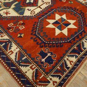 Geometric rug in deep red, navy, and cream with star and medallion motifs on distressed wood flooring.