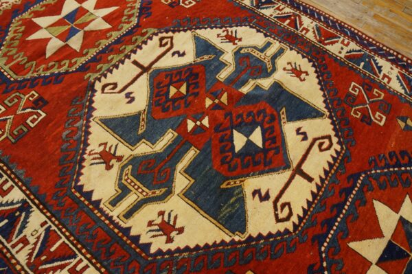 Close-up of a low-pile rug showing red, indigo, and cream geometric tribal patterns on wood flooring.