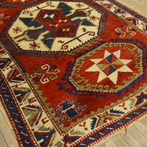 A geometric rug in red, navy, cream, and green sits on distressed wood flooring.