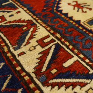 Angled close-up of a dense pile rug showing geometric borders and motifs in red, navy blue, and cream.