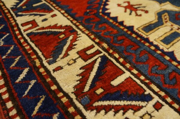 Angled close-up of a dense pile rug showing geometric borders and motifs in red, navy blue, and cream.