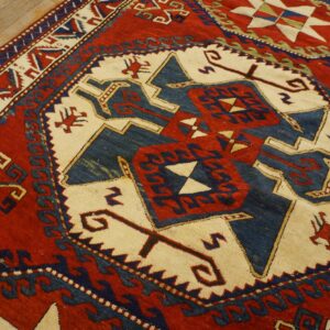 Red, navy, and cream geometric patterned rug with stylized symbols rests on light wood plank flooring.