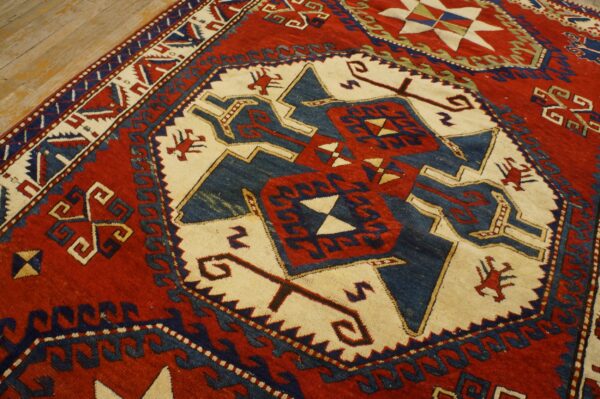 Red, navy, and cream geometric patterned rug with stylized symbols rests on light wood plank flooring.