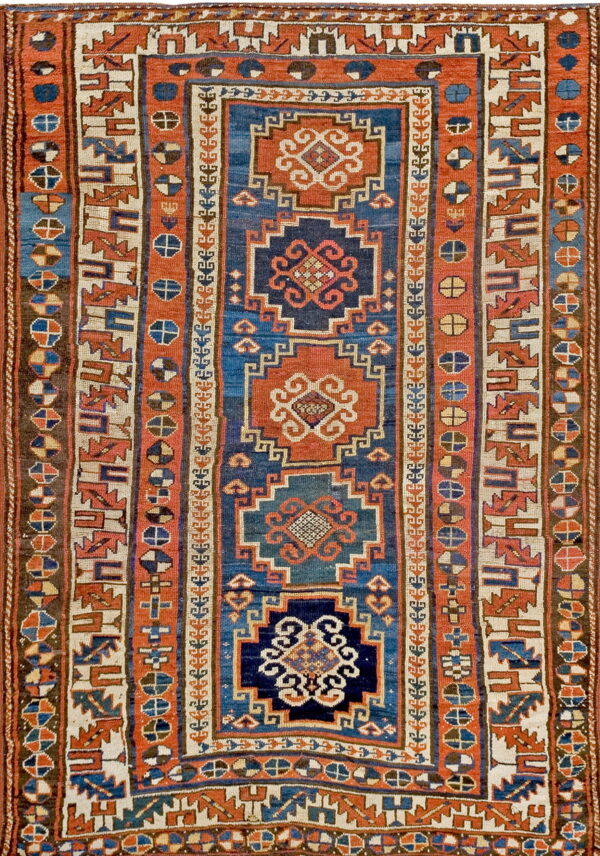 Low-pile rug with central geometric medallions and multiple borders in blue, rust, and cream.
