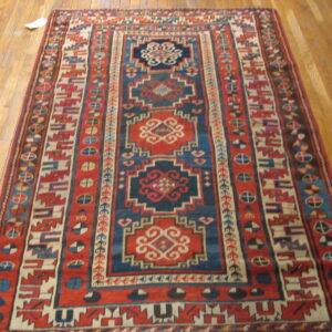 Geometric red and blue rug featuring central medallions and complex borders on light wood flooring.