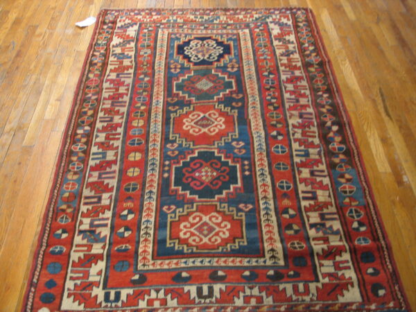 Geometric red and blue rug featuring central medallions and complex borders on light wood flooring.