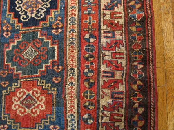 Tightly woven rug with bold geometric patterns in red, navy, teal, and cream on a wooden floor.