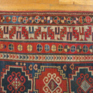 Red and blue geometric rug featuring intricate borders and low pile texture on wooden planks.
